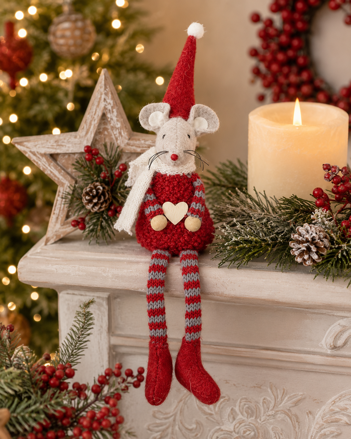 A festive handmade mouse doll with a red knit sweater, striped legs, and a Santa hat, posed on a decorated Christmas mantel with a candle, star ornament, and holiday greenery.