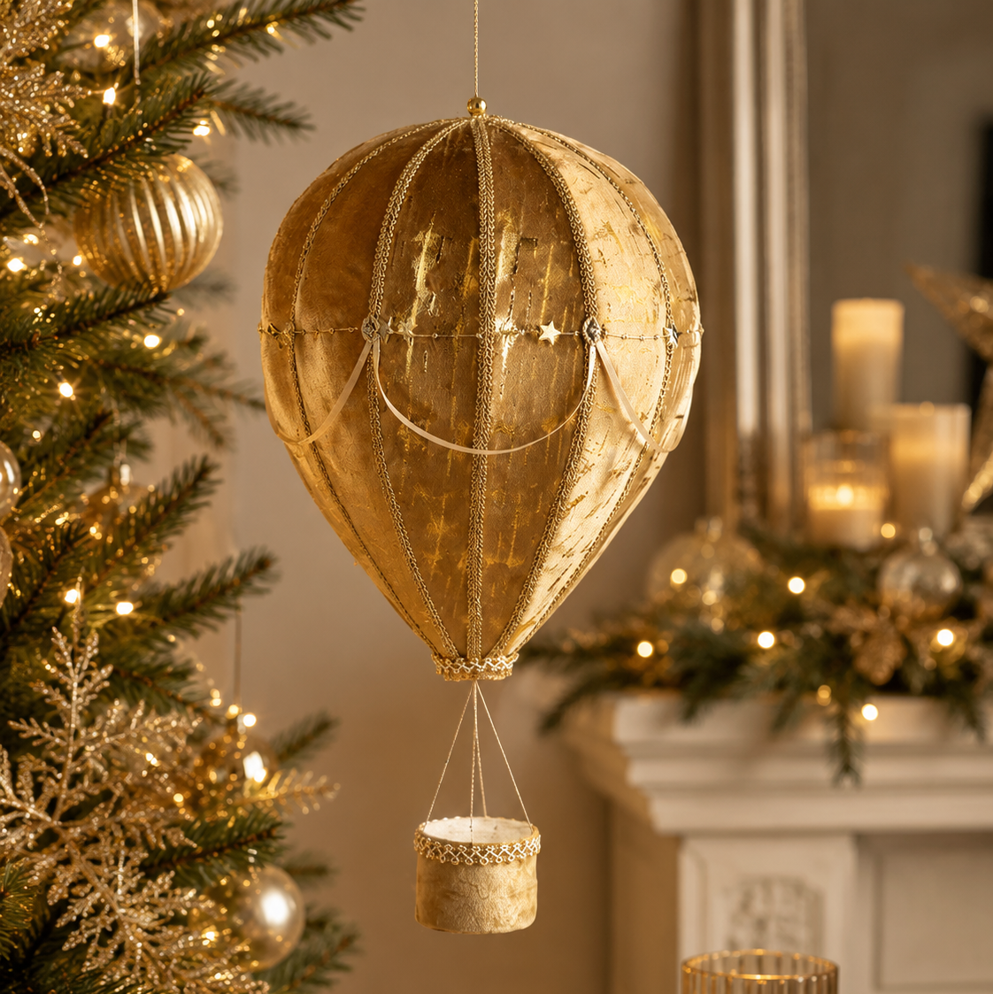 A gold metallic hot air balloon Christmas ornament hanging in front of a decorated Christmas tree and fireplace mantel with warm lit candles.